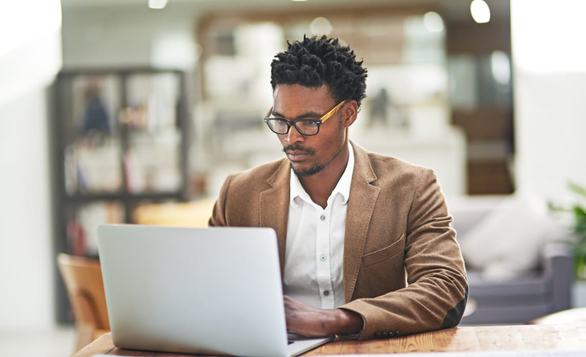 A man sits at a table working on a laptop computer.