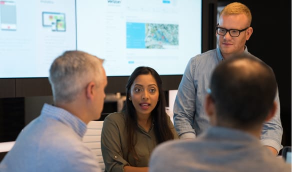 A group of coworkers talk in front of a projected presentation. 