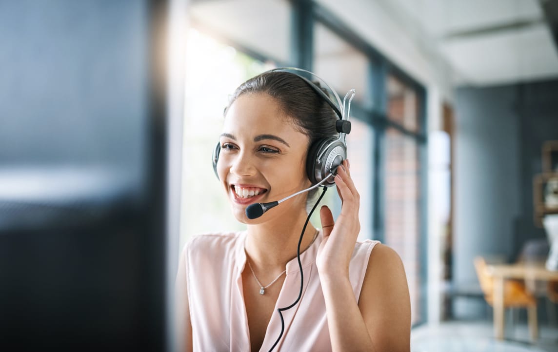  A customer service representative wearing a headset smiles while helping a customer with their phone credit.