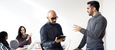 Two men are deep in discussion, one typing on a tablet.