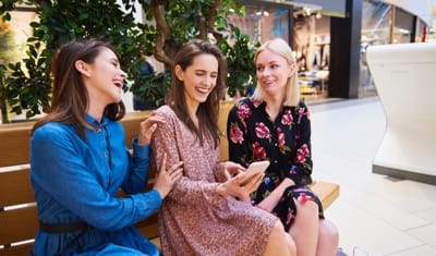 Women at mall sitting on bench looking at phone