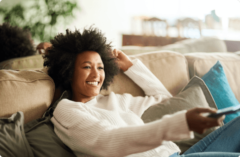 A girl with on a couch with a remote, changing the channel