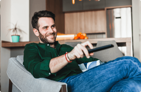 A man on a couch with a remote, changing the channel