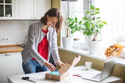 A woman opens a box next to a laptop