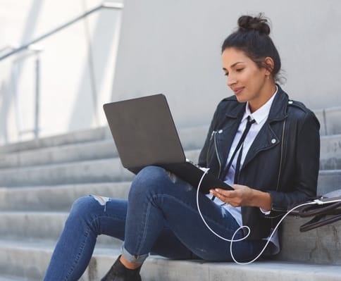 A woman uses her laptop while seated on some steps.