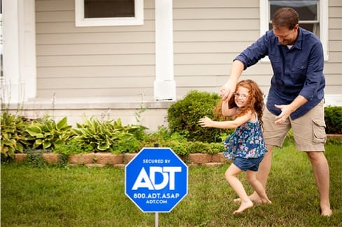 Dad and daughter playing in front yard with ADT sign